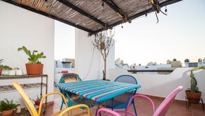 Una terraza con mesa y sillas, plantas en macetas y vistas a edificios.