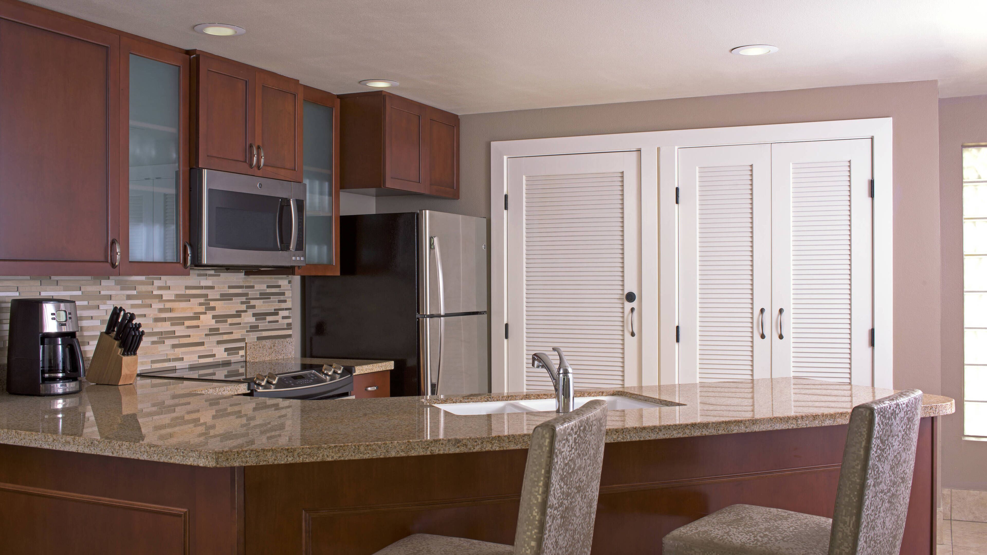 A kitchen with wooden cabinets, a stainless steel refrigerator, a microwave, a coffee maker, and a sink.