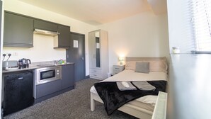 Une chambre d’hôtel compacte comprenant un coin cuisine, un lit et une table de chevet avec une lampe.