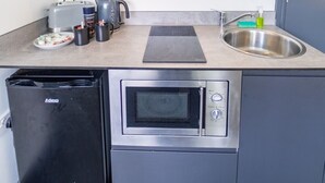Une cuisine compacte avec des meubles gris, un four encastré, un four à micro-ondes, un grille-pain et un évier.