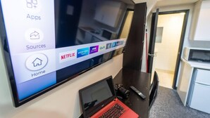 A hotel room with a large flat-screen TV mounted on the wall displaying a TV interface with app icons. - Ensuite style Studio in Selly Oak (Birmingham)