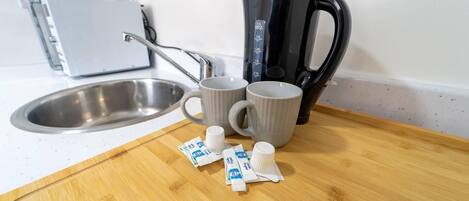 A kitchen counter with a coffee maker, two mugs, and packets of coffee creamer.