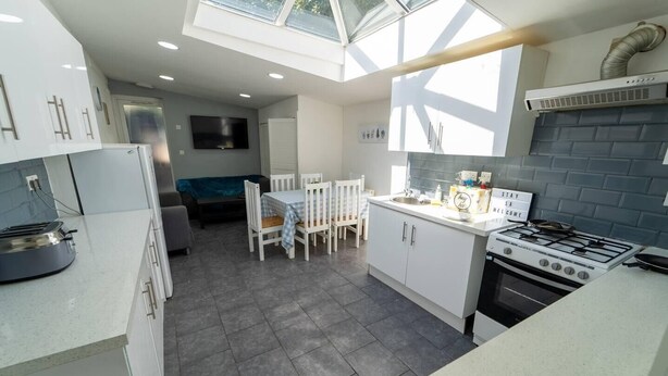 A modern kitchen with a gas stove, a built-in oven, and a dining area with a table and chairs. - Ensuite style Studio in Selly Oak (Birmingham)
