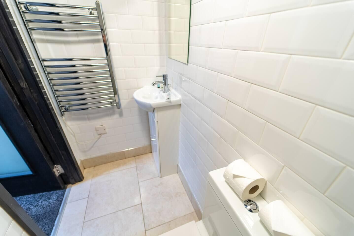 Un baño con paredes de azulejos blancos, un lavamanos, un inodoro y un perchero para toallas.