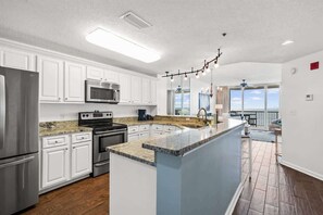 Kitchen features a large island with a granite countertop and stainless steel appliances, including a refrigerator, microwave, and oven.