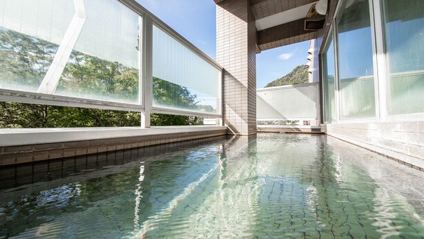 Una piscina interior moderna con agua cristalina, rodeada de grandes ventanales y suelo de baldosas.