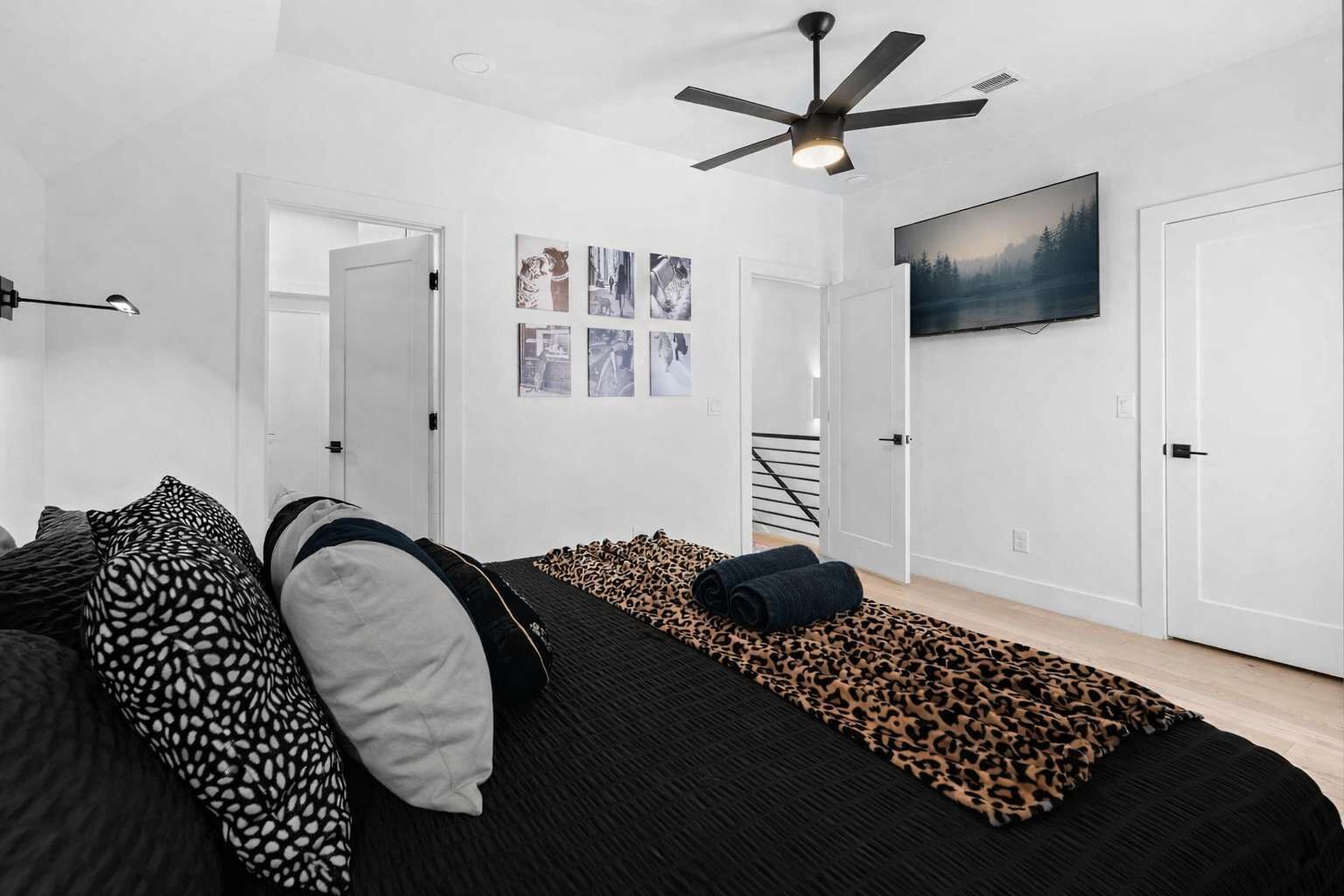 Ein modernes Schlafzimmer mit einer schwarzen Couch, einem Leopardenfell-Teppich und einem Deckenventilator.