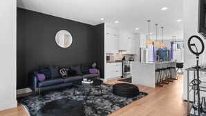 A modern living room with a dark wall, a round mirror, a black leather sofa, and a coffee table. - Stylish Nashville Stay • Skyline Views (Nashville)