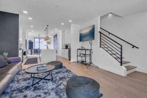 A modern living room with a sofa, coffee table, ottoman, and a staircase.