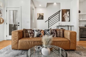 Ein modernes Wohnzimmer mit einem braunen Ledersofa, einem Glastisch mit Dekoration und einer Treppe mit schwarzer Handläufung.