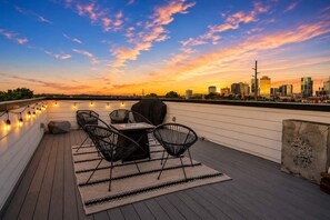 Een terras op het dak met een tafel, stoelen, een barbecue, en uitzicht op de skyline bij zonsondergang.