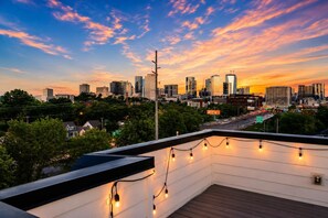 Une terrasse sur le toit, illuminée de guirlandes lumineuses, d’où l’on peut admirer le panorama d’une ville au coucher du soleil.