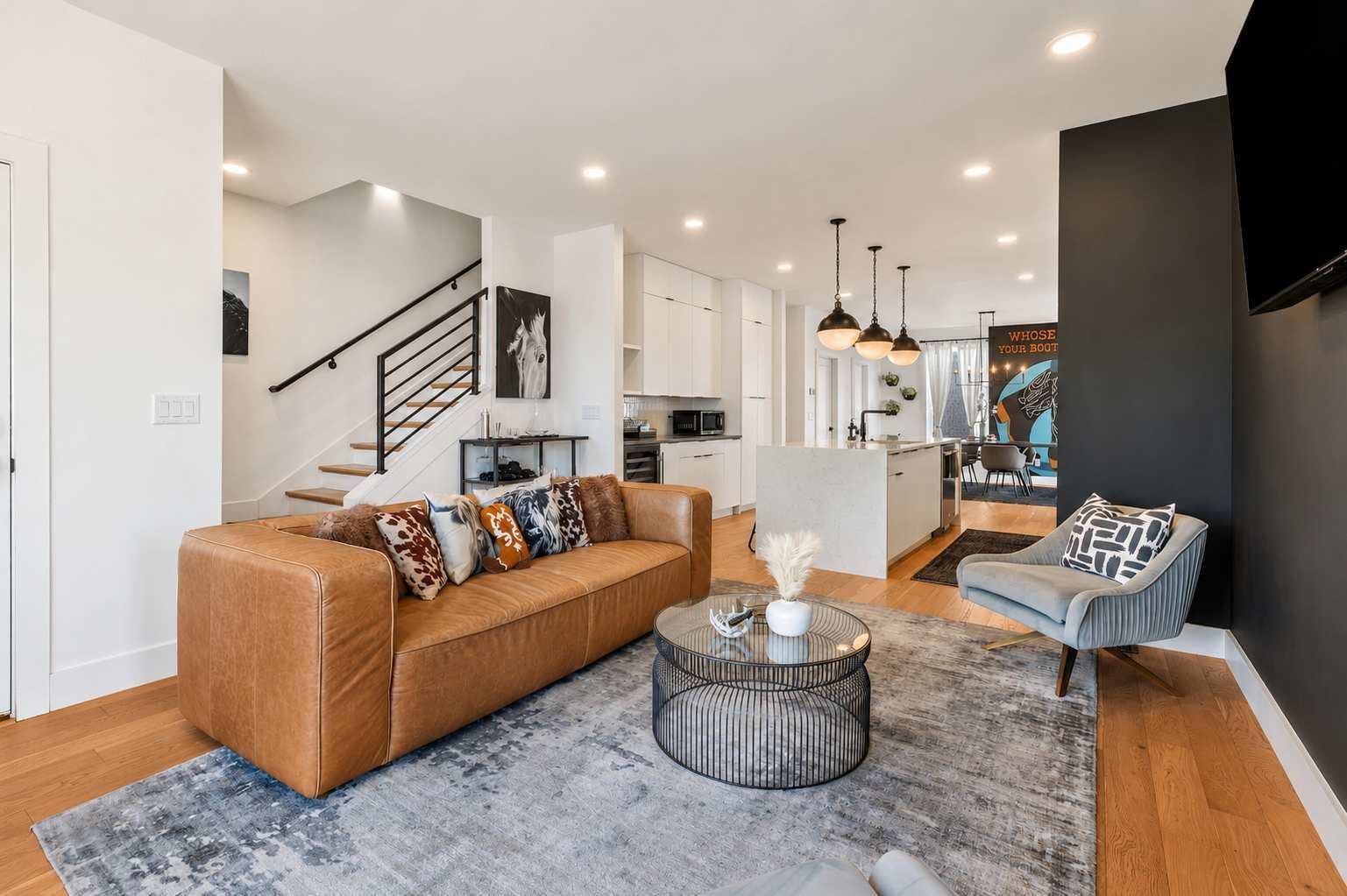 A modern living room with a sofa, a coffee table, and a chair. There is a staircase leading to an upper level.