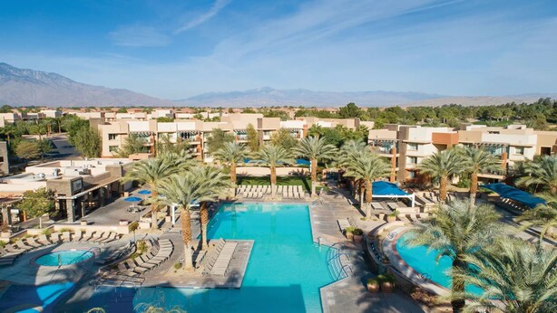 Ein Resort mit zentralem Pool, Palmen und einem Bergpanorama.