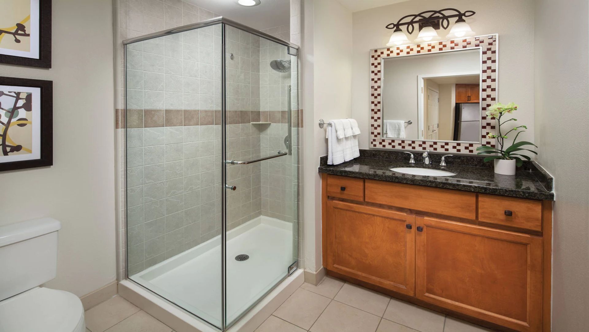 Une salle de bain moderne dotée d’une douche à parois de verre, d’un lavabo avec un plan de travail en marbre, de meubles en bois et d’un sol carrelé.