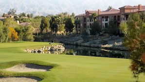 A golf course with a pond, a person playing golf, and a building with a red roof in the background. - Studio - Marriott's Shadow Ridge II - The Enclaves - Full Resort Access (Palm Desert)