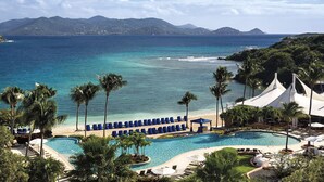 Un complexe hôtelier doté d’une piscine, de chaises longues, de palmiers et offrant une vue sur la mer et les montagnes.