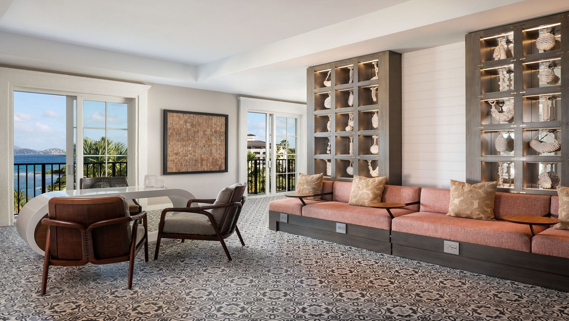 A modern living room with a large sofa, a dining table, and chairs. There is a large window with a view of the sea.