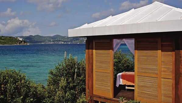 A wooden cabin with a bed, a view of the sea, and mountains in the background. - 3 Bedroom - The Ritz-Carlton Club, St. Thomas - Full Resort Access (St Thomas)