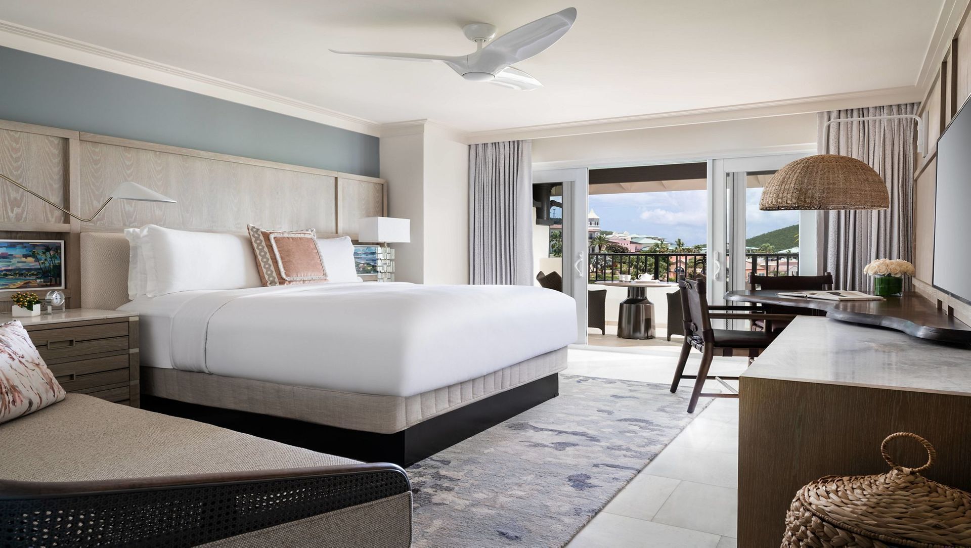 Une chambre d’hôtel équipée d’un lit, d’un bureau, d’une chaise, d’un balcon avec vue et d’un ventilateur de plafond.