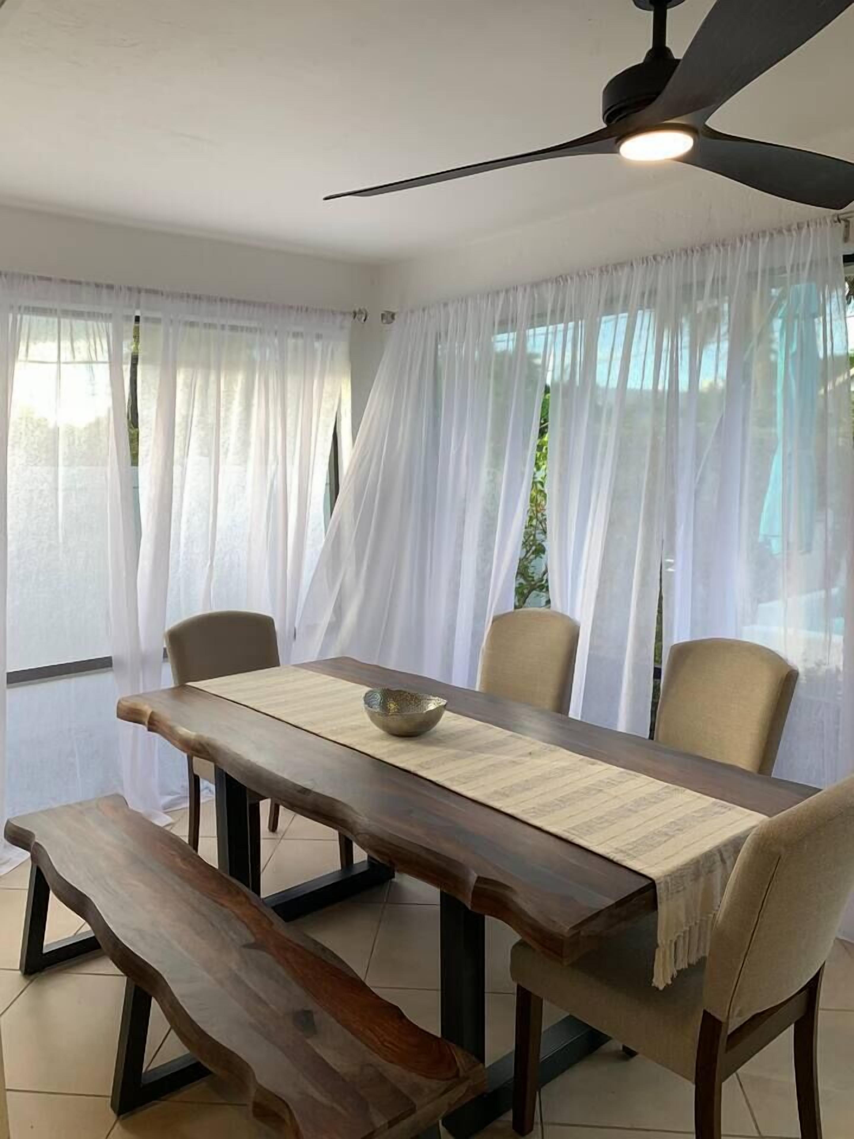 Un comedor con una mesa de madera, cuatro sillas, un banco y un ventilador de techo.