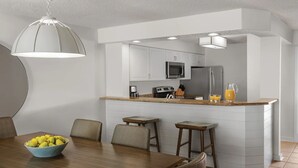 Una cucina moderna con mobili bianchi, un'isola centrale con sgabelli, un tavolo da pranzo con sedie e una lampada a sospensione.