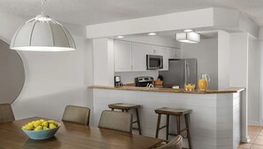Une cuisine moderne avec des meubles blancs, un îlot central doté de tabourets, une table à manger avec des chaises et un luminaire suspendu.