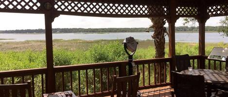 A wooden deck with a telescope, chairs, and a table overlooking a lake.