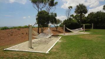 Two hammock setups in a grassy area with trees and a sandy beach in the background.