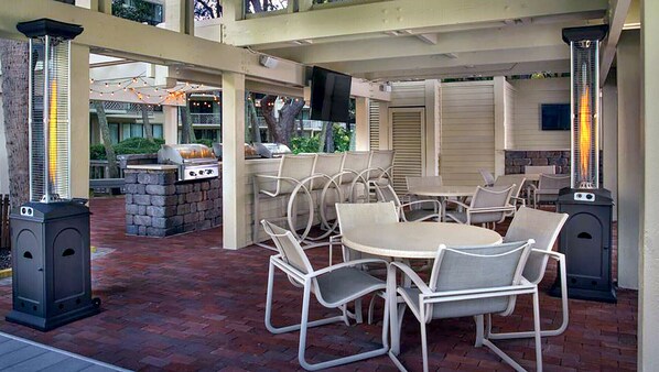 Une terrasse extérieure avec des tables et des chaises rondes, un barbecue et deux appareils de chauffage.