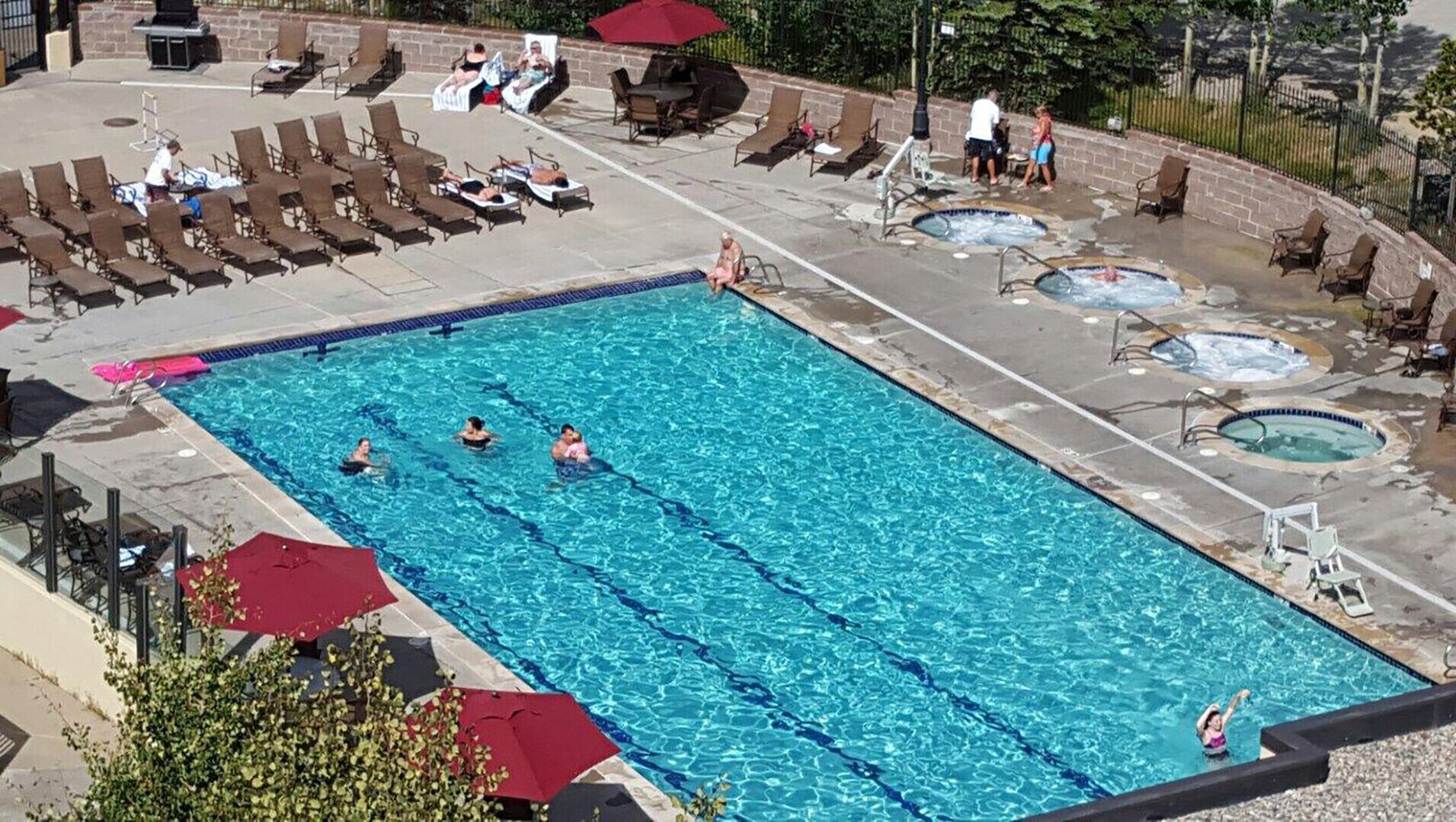 A rectangular swimming pool with clear blue water, surrounded by lounge chairs and a hot tub area.