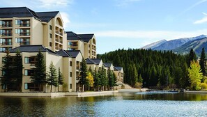 Un hotel a più piani con balconi e vista sul lago, circondato da alberi e montagne.