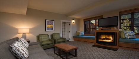 A cozy living room with a fireplace, a sofa, two armchairs, a coffee table, and a television.