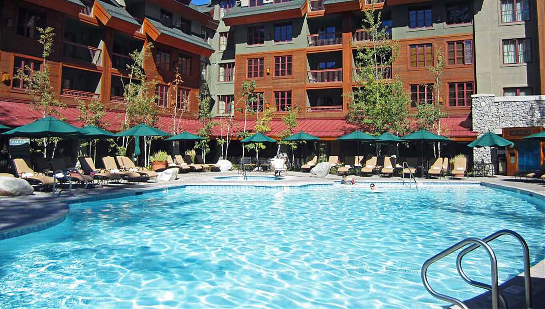 Ein Swimmingpool mit Liegestühlen und Sonnenschirmen, umgeben von mehrstöckigen Gebäuden mit Balkonen.