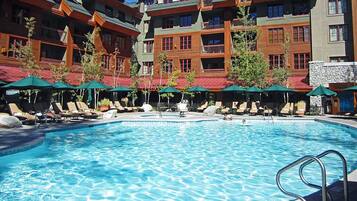 Ein Swimmingpool mit Liegestühlen und Sonnenschirmen, umgeben von mehrstöckigen Gebäuden mit Balkonen.