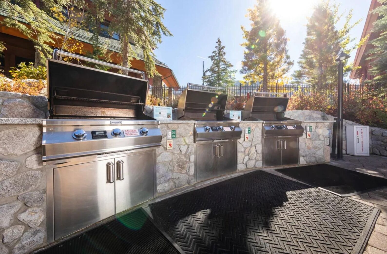 An outdoor barbecue area with two stainless steel grills, stone walls, and a paved entrance.
