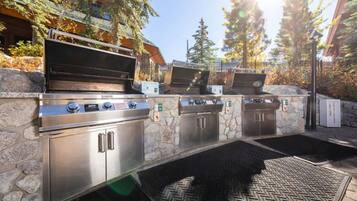An outdoor barbecue area with two stainless steel grills, stone walls, and a paved entrance.