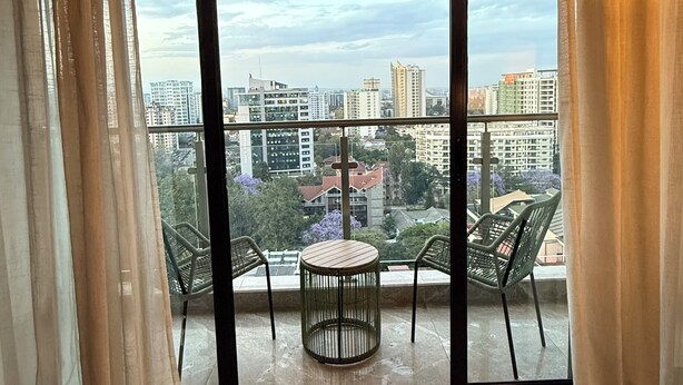 Un balcon avec une table ronde et des chaises, une vue sur le paysage urbain et une porte-fenêtre coulissante.