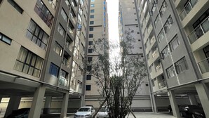Un immeuble résidentiel de grande hauteur, doté de nombreux étages, d’une cour intérieure avec un arbre et de voitures garées.