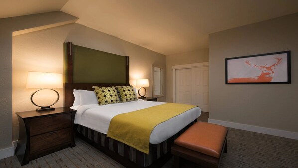 A hotel room with a bed, two bedside tables with lamps, a bench, a mirror, and a framed picture on the wall.
