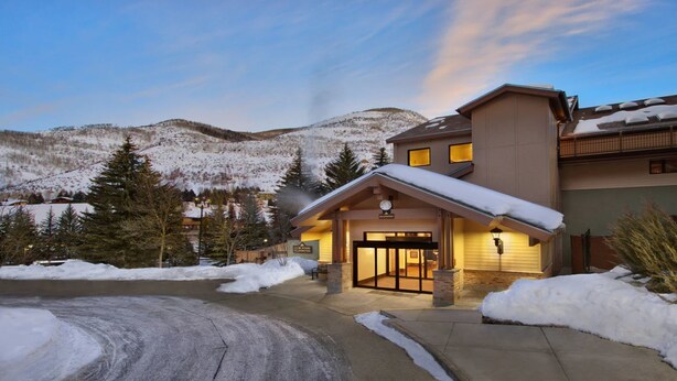 Un chalet dont l’entrée est recouverte de neige, avec une vue sur les montagnes et un ciel dégagé.