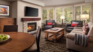 Una sala de estar con chimenea, sillones de cuero, un sofá, una mesa de centro y un televisor montado en la pared.