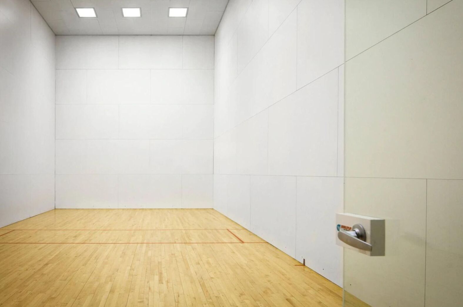 Una habitación amplia y vacía con piso de madera y paredes blancas, que presenta un techo con iluminación empotrada y un enchufe eléctrico en la pared.
