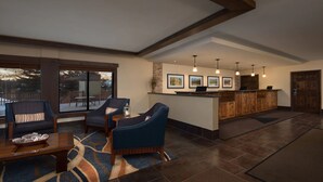 Un vaste espace de vie agrémenté d’une grande fenêtre, d’un comptoir d’accueil en bois et d’un coin salon avec des fauteuils à revêtement bleu.