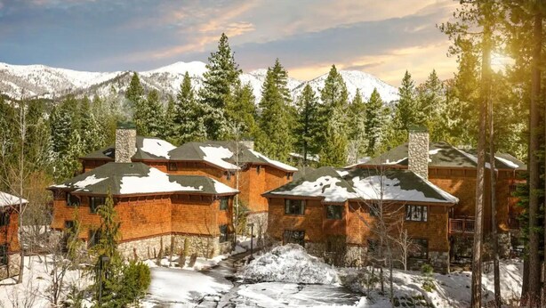 Un chalet doté de plusieurs cabanes en bois, entouré de montagnes et d’arbres couverts de neige.