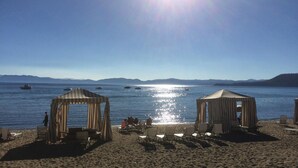 Une plage agrémentée de deux pergolas en bois, de chaises longues et offrant une vue dégagée sur la mer et les montagnes lointaines.