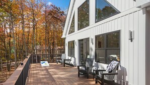 Une terrasse en bois, avec des chaises et une table, donnant sur une forêt aux couleurs automnales.