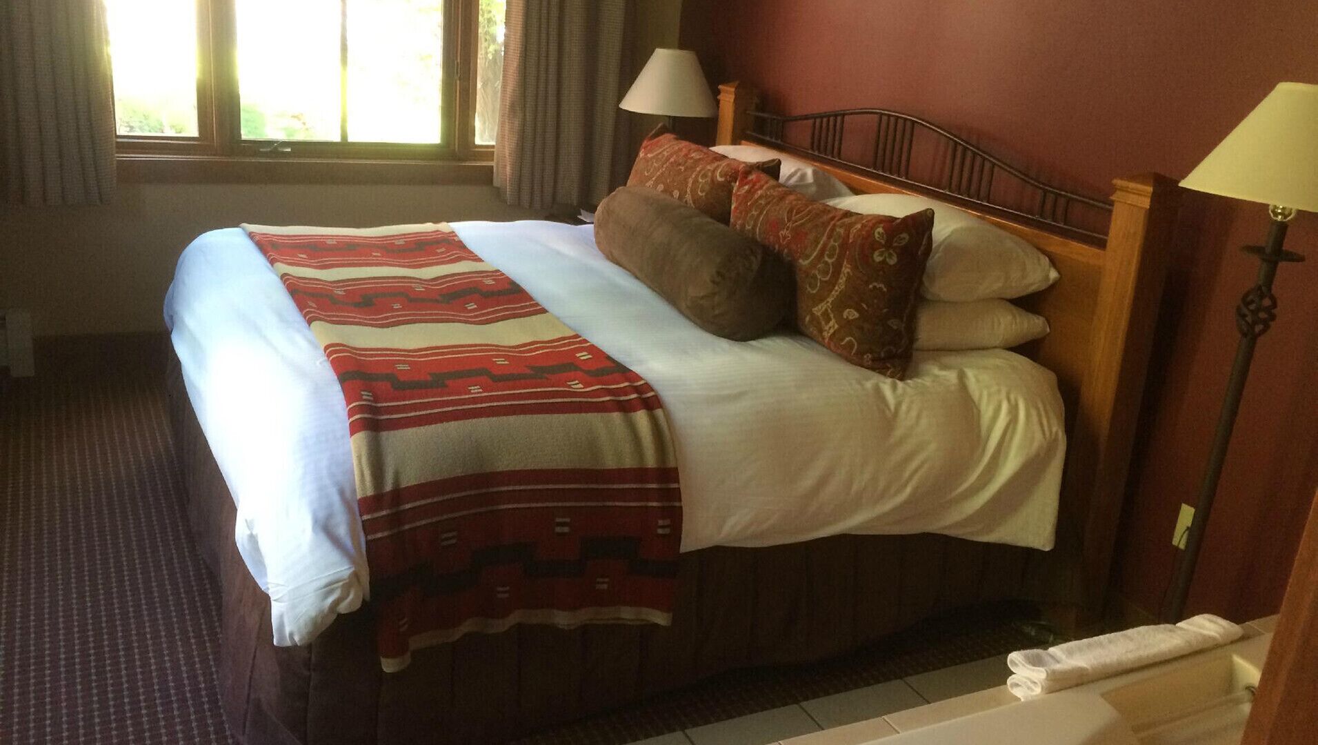A hotel room with a bed, two bedside lamps, a window with curtains, and a view of greenery outside.