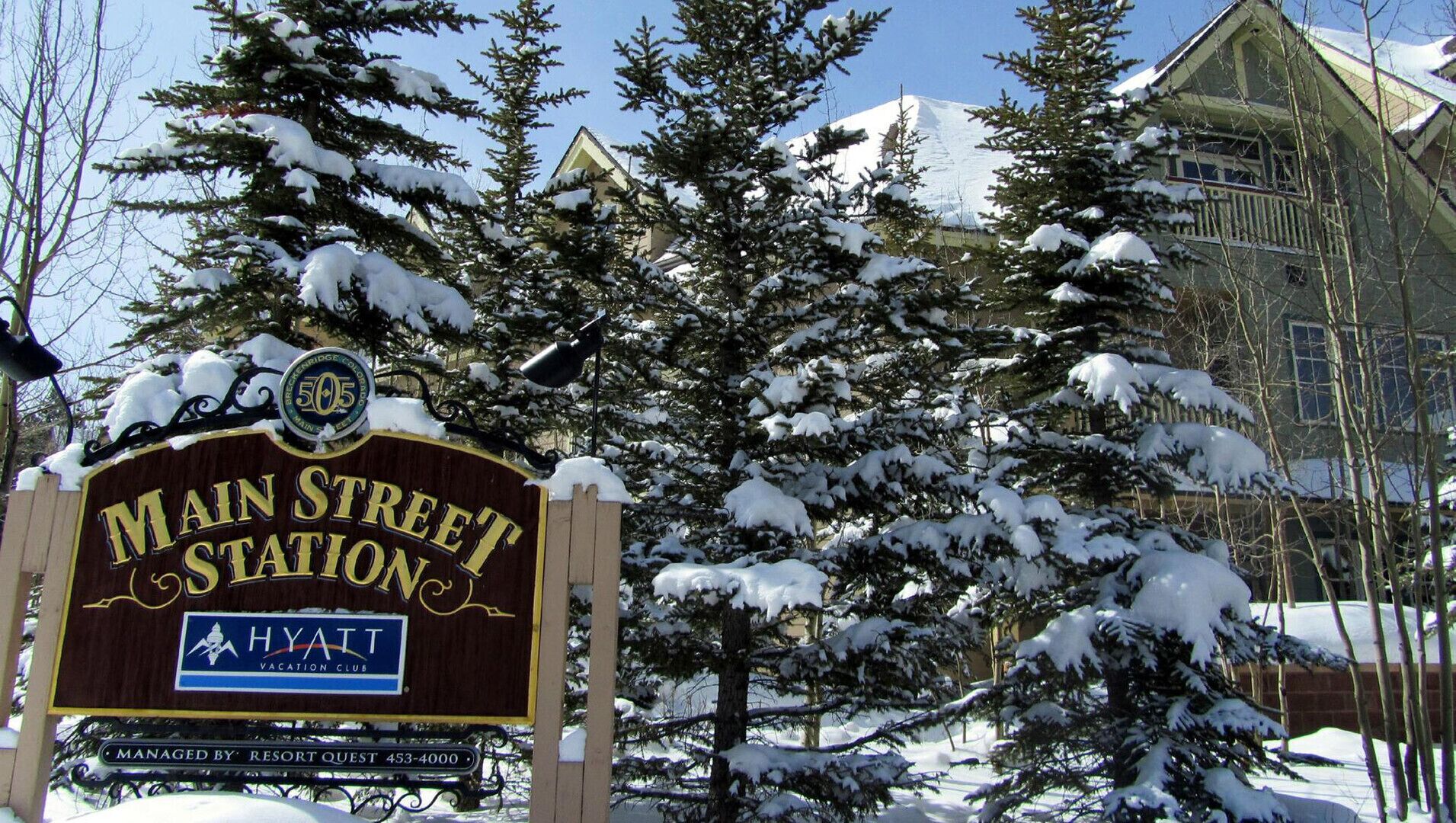 Un panneau recouvert de neige indiquant l’emplacement de la station Main Street, géré par Resort Quest, avec un numéro de téléphone à contacter.