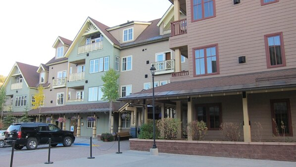 A row of multi-story buildings with balconies, a covered walkway, and a parked SUV.